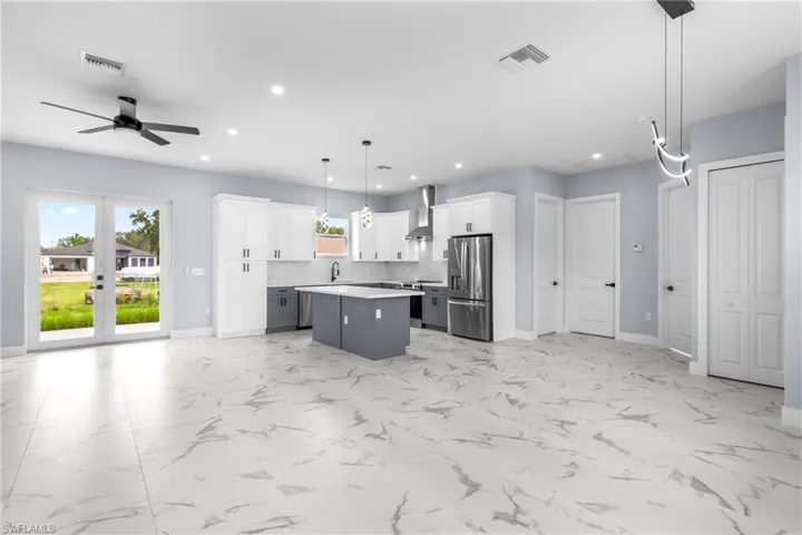 Kitchen featuring hanging light fixtures, gray cabinetry, white cabinets, appliances with stainless steel finishes, and a kitchen island