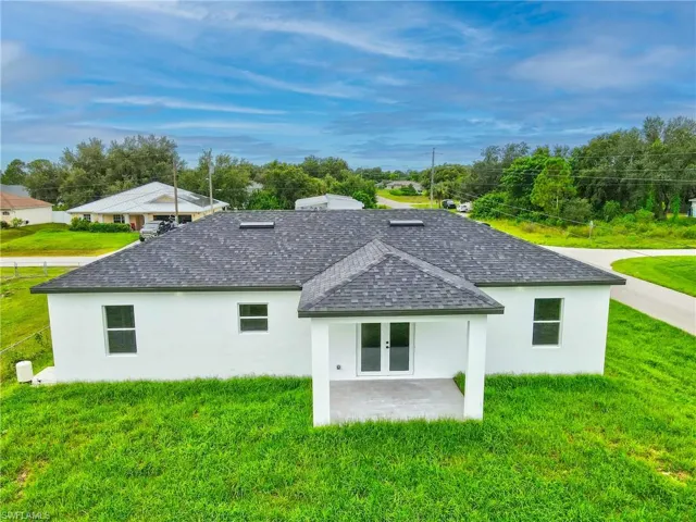 Back of house featuring a shingled roof, a yard, stucco siding, and french doors