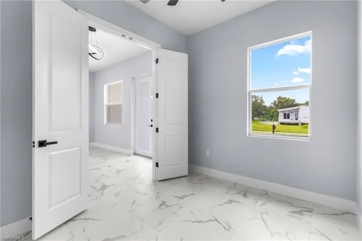 Empty room with healthy amount of natural light, light marble finish floors, and a ceiling fan