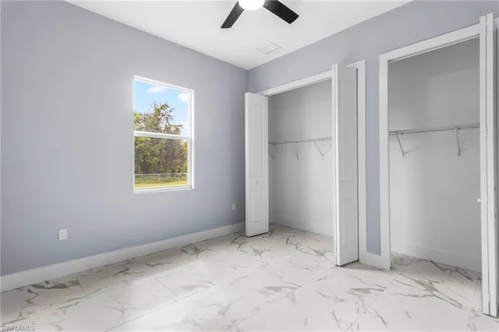 Unfurnished bedroom featuring light marble finish flooring, two closets, and ceiling fan