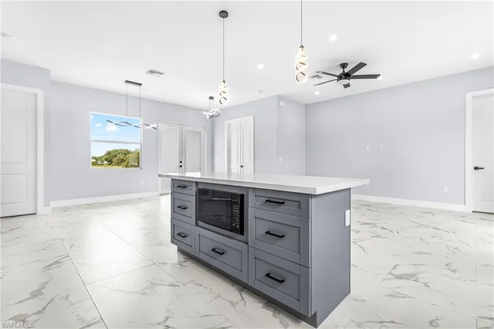 Kitchen featuring a ceiling fan, decorative light fixtures, a center island, black microwave, and light marble finish floors