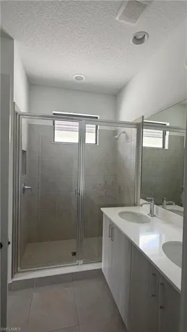 Enclosed glass shower with tiled walls and floor, complemented by a double vanity featuring integrated sinks and contemporary cabinetry
