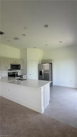 Modern kitchen featuring a breakfast bar with a white countertop, stainless steel appliances, light-toned cabinetry, and recessed lighting