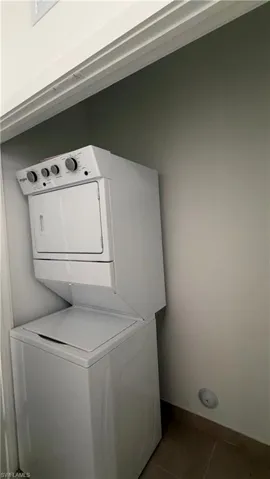 White stacked washer and dryer unit within a dedicated alcove, featuring a light-toned wall and complementary floor tiling