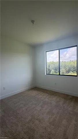 Interior room featuring neutral-toned carpet flooring, white painted walls, and a large window with black framing