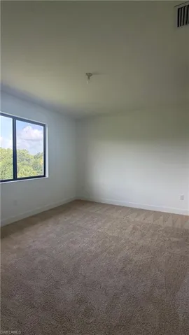 Spacious room featuring neutral carpeting, white walls, clean baseboards, and a large window