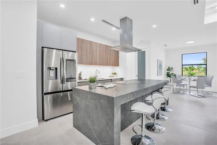 Kitchen with dark stone counters, stainless steel refrigerator with ice dispenser, a kitchen bar, a kitchen island, and island range hood