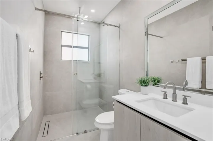 Bathroom featuring tile walls, a shower with door, toilet, and vanity