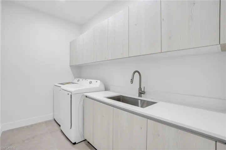 Washroom with sink, cabinets, washing machine and dryer, and light tile patterned floors