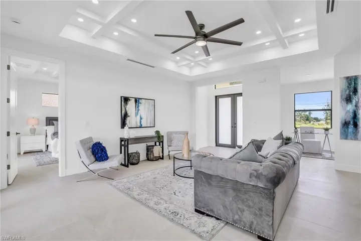 Living room featuring light tile patterned flooring, beam ceiling, coffered ceiling, and ceiling fan