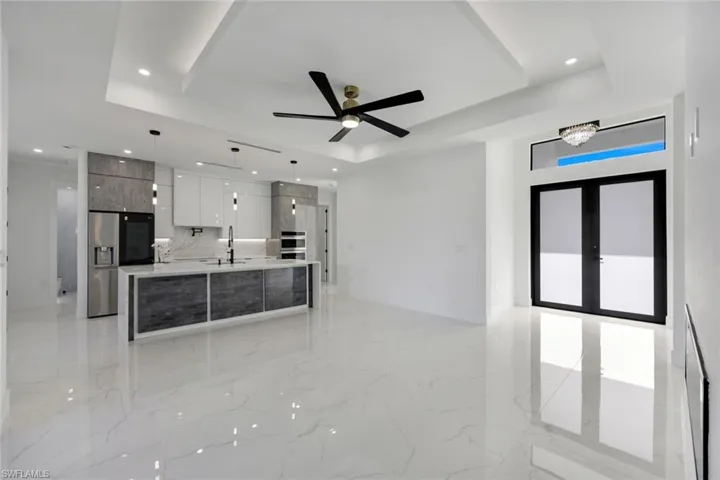Kitchen featuring pendant lighting, a tray ceiling, a kitchen island with sink, and white cabinets