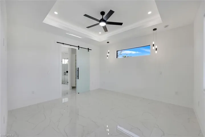 Unfurnished room featuring a tray ceiling, a barn door, and ceiling fan