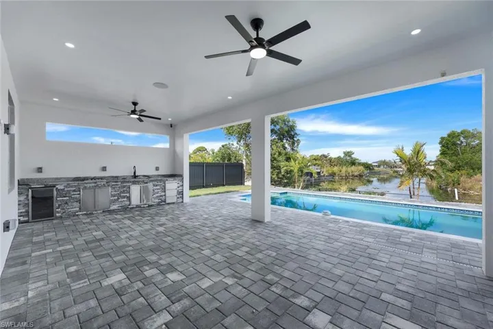 View of pool featuring an outdoor kitchen, sink, a patio area, a water view, and ceiling fan