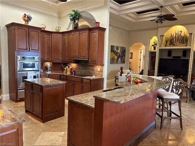 Kitchen featuring sink, coffered ceiling, double oven, a center island with sink, and ornamental molding