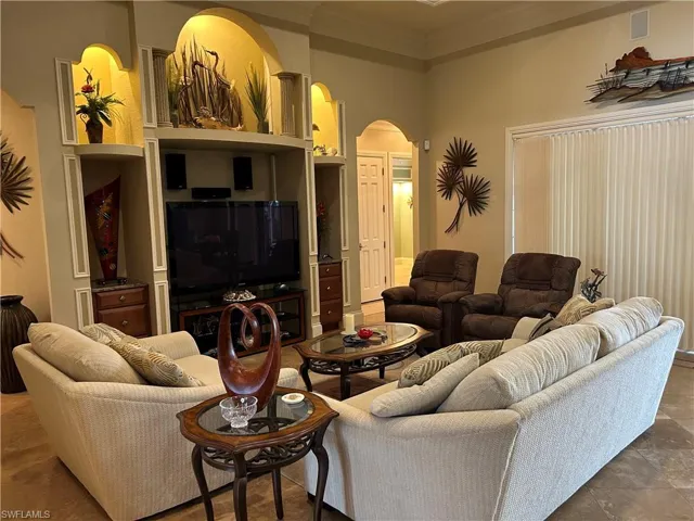 Living room with built in TV area, stacking sliders with pool and lake view, crown and coffered ceiling.