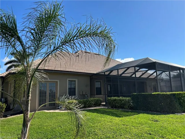 Rear view looking left of property with French doors from 3rd garage, pool cage and a lawn.
