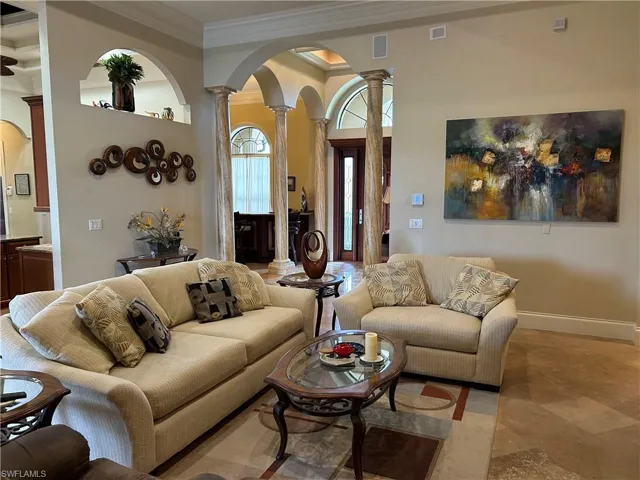 Living room looking towards entrance but includes a built in TV area, stacking sliders with pool and lake view, crown and coffered ceiling.