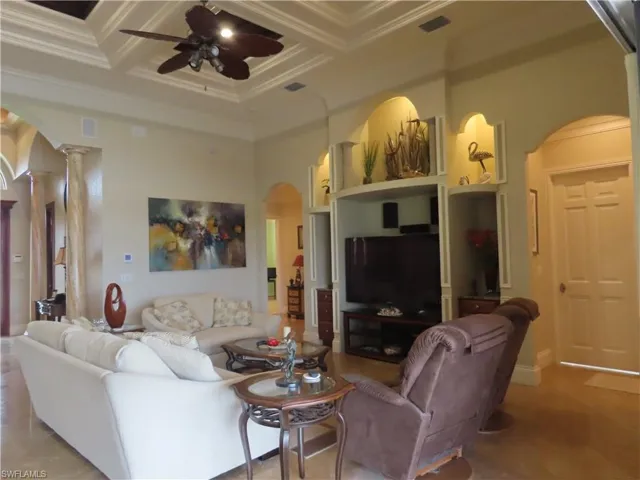 Living room looking toward bedroom entrances, which includes the built in TV area, stacking sliders with pool and lake view, crown and coffered ceiling.