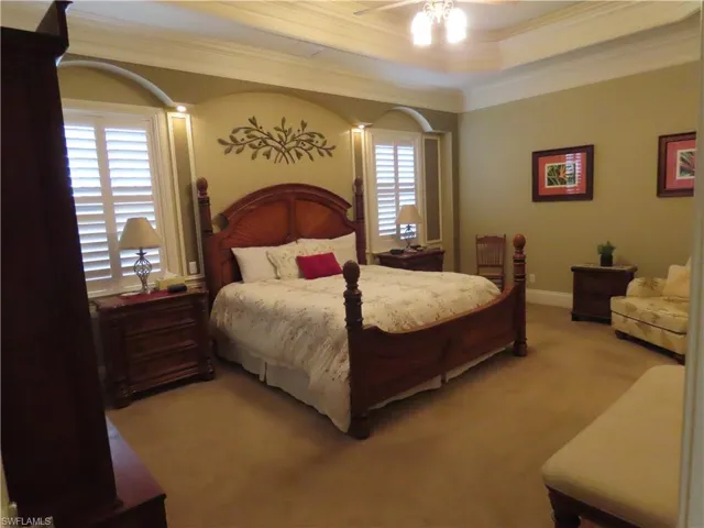 Master bedroom with plantation shuttered windows, ceiling fan, tray ceiling with crown molding.