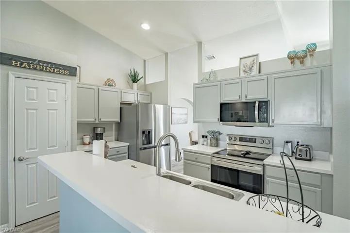 Kitchen featuring appliances with stainless steel finishes, light hardwood / wood-style floors, sink, and vaulted ceiling