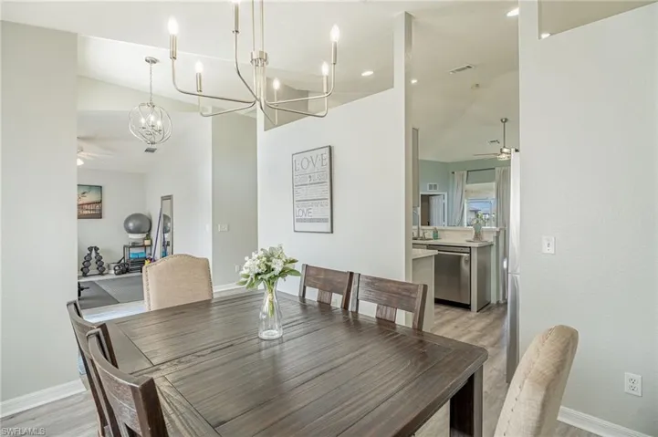 Dining room with lofted ceiling, light hardwood / wood-style flooring, and ceiling fan with notable chandelier