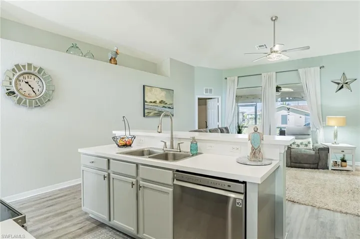 Kitchen with light hardwood / wood-style flooring, a center island with sink, ceiling fan, stainless steel dishwasher, and sink