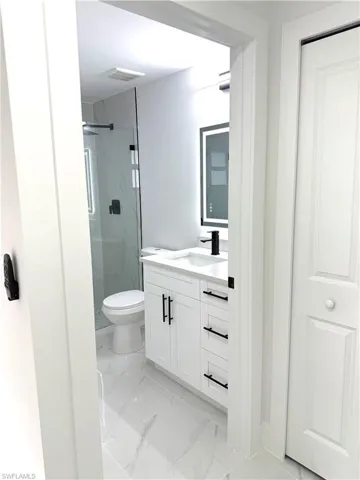 Bathroom with vanity, a marble finish shower, and light marble finish floors