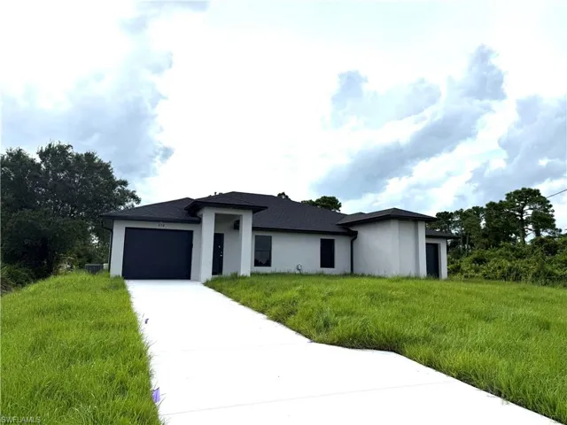Prairie-style house with an attached garage, driveway, stucco siding, and a front yard