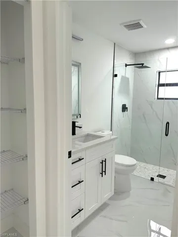 Bathroom featuring vanity, a marble finish shower, light marble finish floors, and a walk in closet