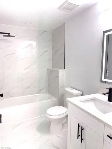 Bathroom with vanity, a combined bath / shower with marble appearance, and light marble finish flooring