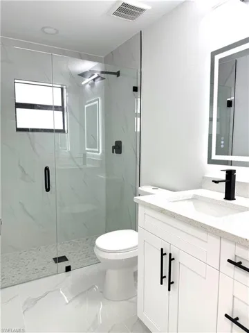 Full bath featuring vanity, a marble finish shower, and light marble finish floors
