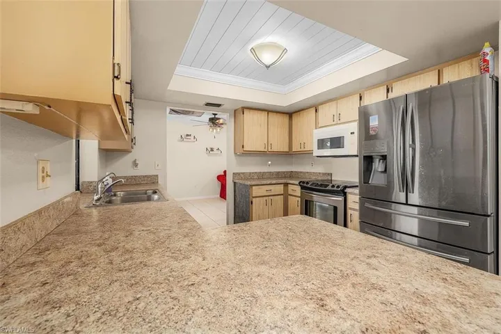 Kitchen with ceiling fan, a tray ceiling, sink, appliances with stainless steel finishes, and light tile patterned floors