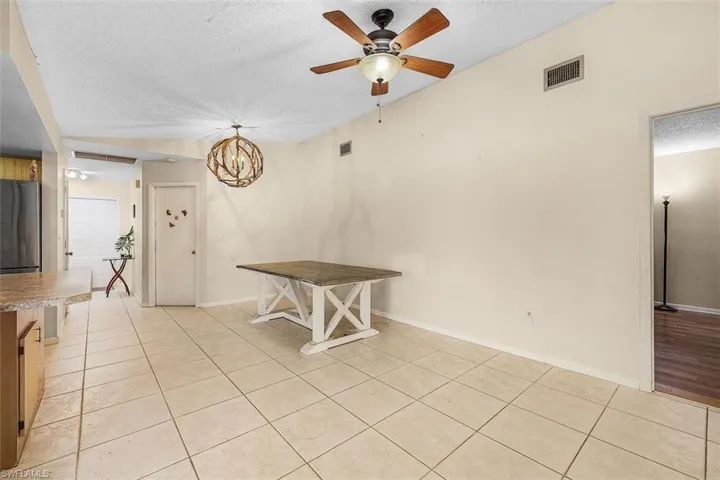 Unfurnished dining area featuring ceiling fan with notable chandelier, light wood-type flooring, and a textured ceiling