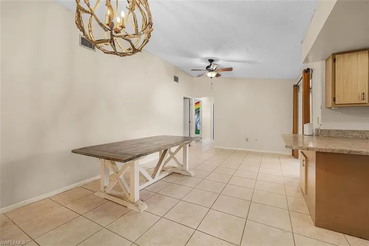 Unfurnished dining area with ceiling fan with notable chandelier, light tile patterned floors, and a textured ceiling
