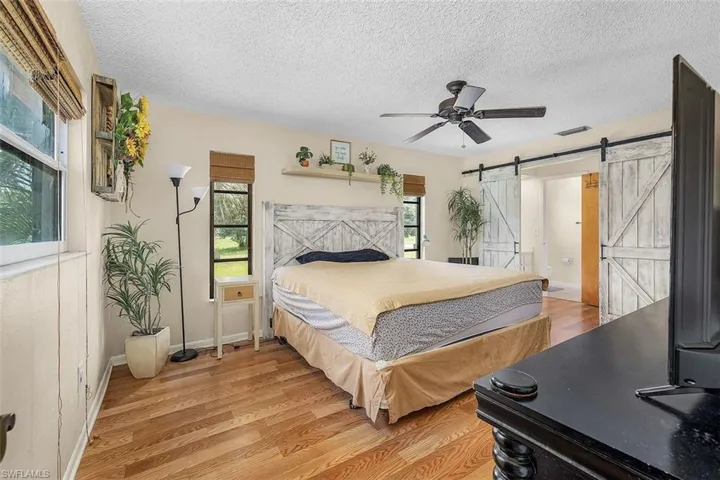 Bedroom with light hardwood / wood-style flooring, a barn door, a textured ceiling, and ceiling fan