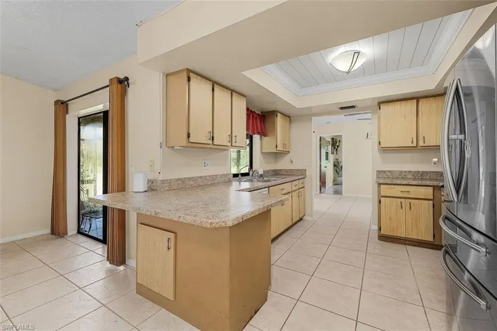 Kitchen with stainless steel fridge, light brown cabinets, light tile patterned floors, crown molding, and a tray ceiling