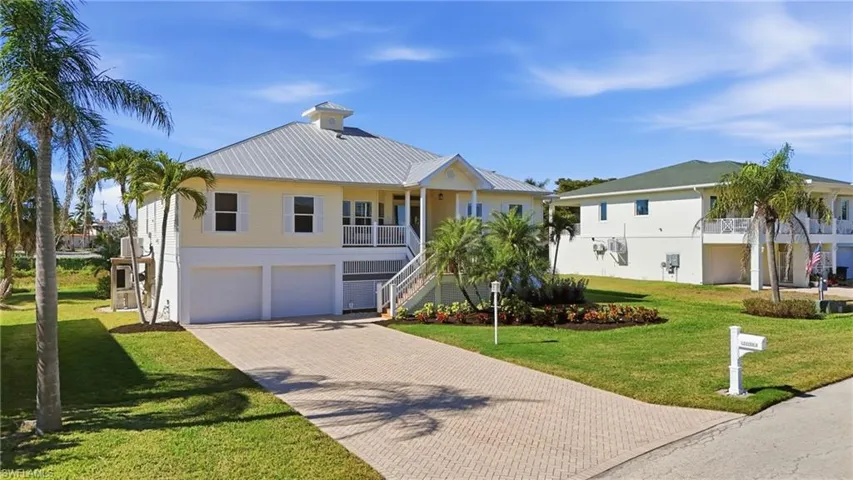 Coastal inspired home featuring stairway, a front lawn, a metal roof, decorative driveway, and a garage - Virtually Edited