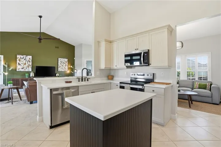 Kitchen featuring open floor plan, high vaulted ceiling, light countertops, appliances with stainless steel finishes, and a center island - Virtually Edited