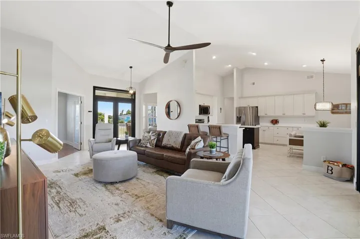 Living area with high vaulted ceiling, a ceiling fan, and light tile patterned floors - Virtually Edited