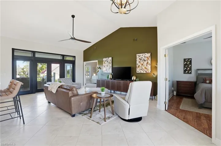Living room featuring high vaulted ceiling, a ceiling fan, light tile patterned floors, and french doors - Virtually Edited