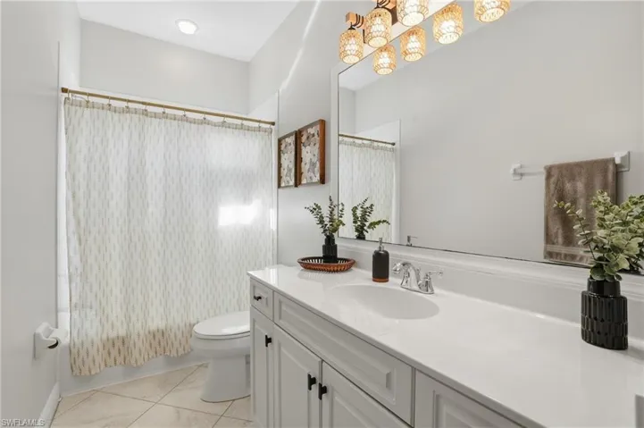 Full bathroom with vanity, shower / bathtub combination with curtain, a chandelier, and light tile patterned flooring - Virtually Edited