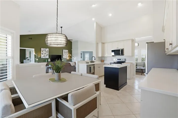Dining area with high vaulted ceiling, a chandelier, and light tile patterned floors - Virtually Edited