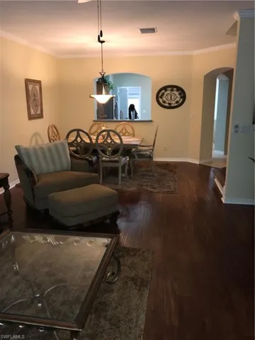 Dining area with arched walkways, dark wood-style flooring, and crown molding