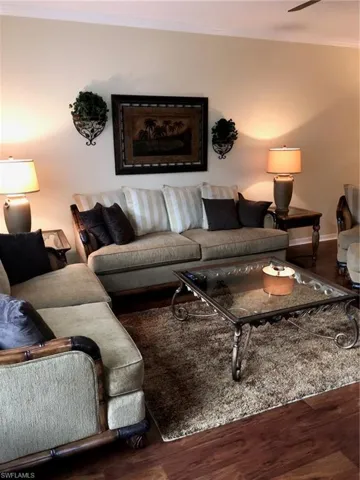 Living room with crown molding, dark wood-type flooring, and a ceiling fan