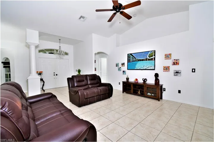 Living room featuring ceiling fan, light tile patterned floors, high vaulted ceiling, and decorative columns