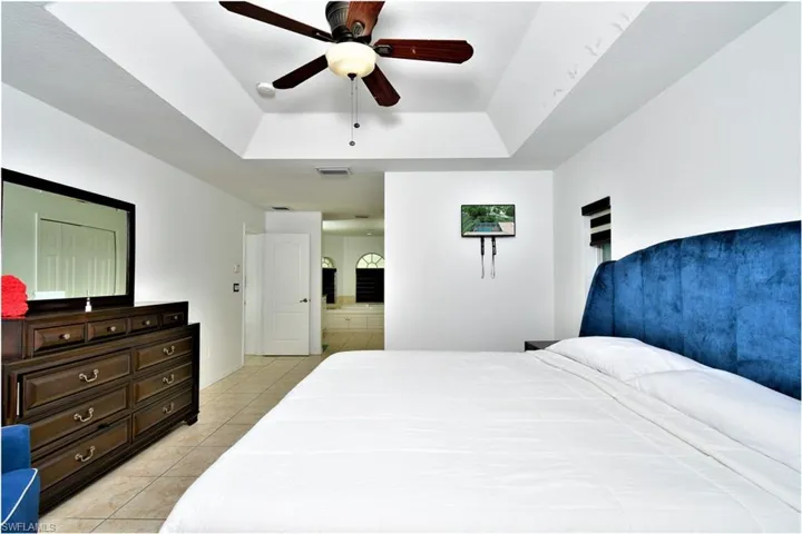 Tiled bedroom featuring a raised ceiling and ceiling fan