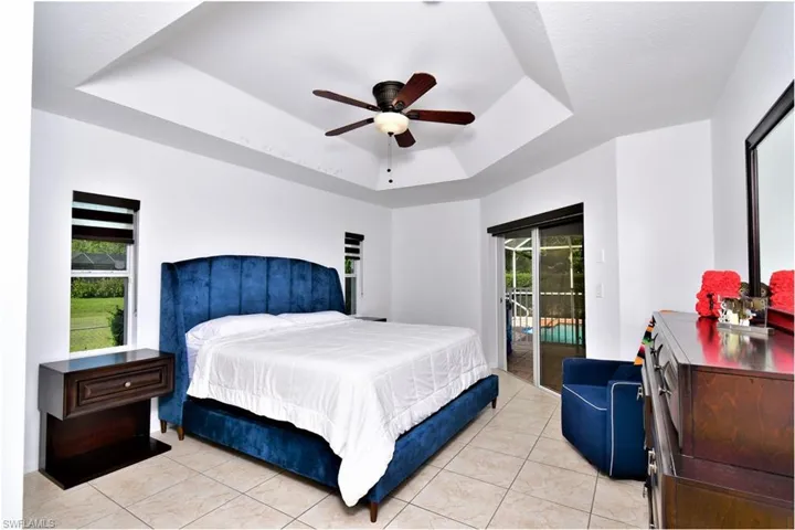 Tiled bedroom featuring access to exterior, ceiling fan, multiple windows, and a tray ceiling