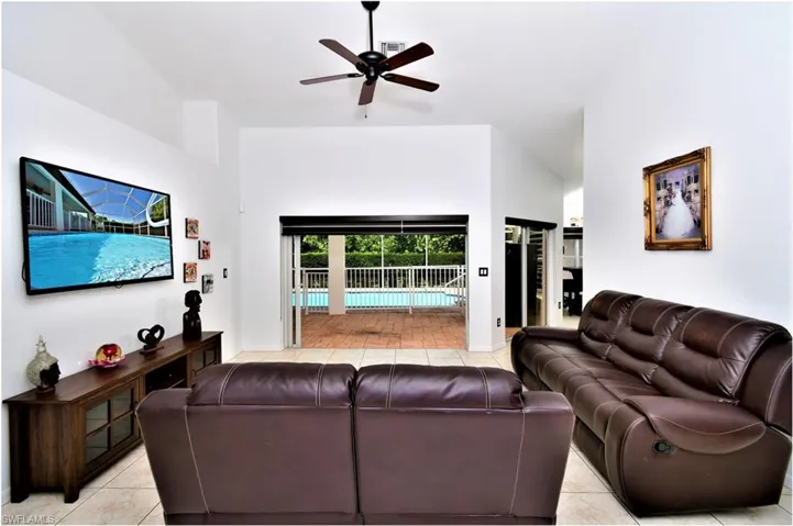 Living room with vaulted ceiling, light tile patterned floors, and ceiling fan