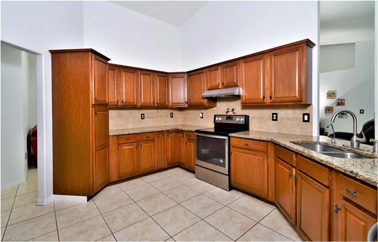 Kitchen with light tile patterned floors, stainless steel electric range, sink, decorative backsplash, and light stone counters