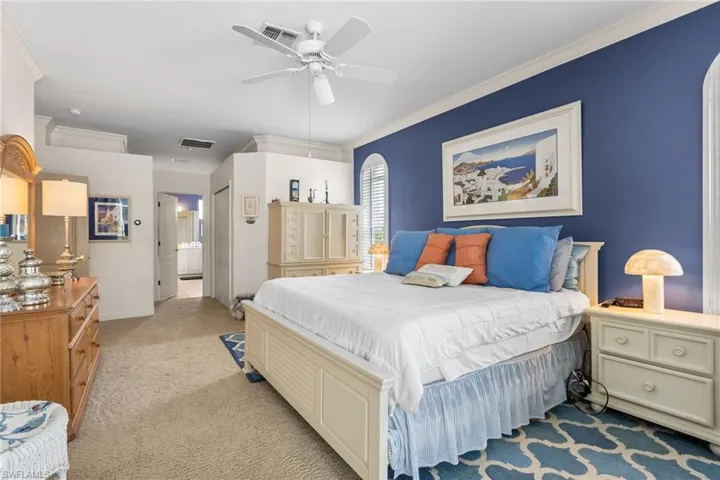 Bedroom with visible vents, light colored carpet, ensuite bath, and ornamental molding
